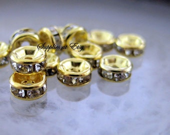 May include: A group of gold-toned metal bead caps with clear rhinestone accents. The bead caps are arranged in a cluster on a white surface.