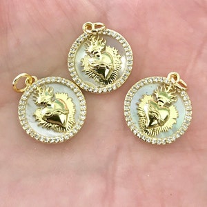 Peut inclure: Trois pendentifs dor&eacute;s avec un fond en nacre blanche et un motif de c&oelig;ur en or. Chaque pendentif est entour&eacute; d'un cercle de strass transparents.