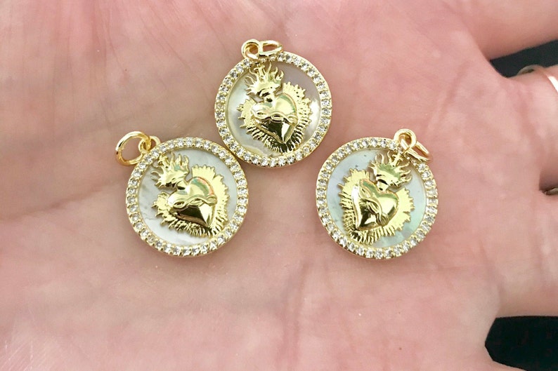 Peut inclure: Trois pendentifs dor&eacute;s avec un fond en nacre blanche et un motif de c&oelig;ur en or. Chaque pendentif est entour&eacute; d'un cercle de strass transparents.