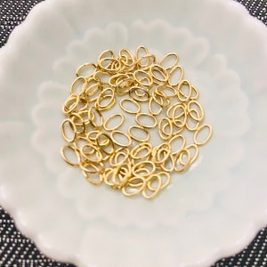 May include: A white bowl filled with a large quantity of small, gold-colored oval jump rings.