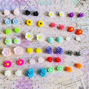 May include: Assortment of colourful flower-shaped earrings. The earrings are made of plastic and come in a variety of colours, including pink, blue, yellow, green, red, and purple. The earrings are arranged in rows on a white background.