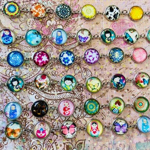 May include: A collection of colorful charm bracelets with various designs, including butterflies, flowers, and Russian nesting dolls. The bracelets are made with silver-toned metal chains and round glass charms.