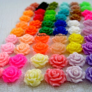 May include: Assortment of colourful plastic rose flower embellishments. The roses are arranged in rows by colour, starting with red and ending with purple. The roses are approximately 1 inch in diameter.