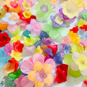 Pode incluir: Conjunto de contas de flores de plástico coloridas em vários tons de rosa, roxo, amarelo, verde, azul e vermelho. As contas são translúcidas e têm um acabamento brilhante.