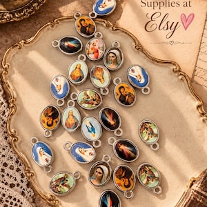 May include: A collection of oval-shaped metal charms featuring various religious imagery, including depictions of the Virgin Mary and Jesus Christ. Each charm has a small loop at the top and bottom, with colorful printed icons set within silver-toned frames.
