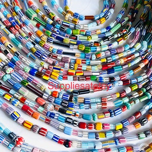 May include: A collection of colorful glass beads, some with stripes and some with solid colors. The beads are arranged in rows, with the largest beads at the top and the smallest beads at the bottom. The beads are all different sizes and shapes, and they are all very bright and colorful.