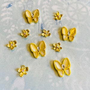Puede incluir: Surtido de charms para uñas de mariposa y flor en tono dorado. Las mariposas tienen alas iridiscentes y detalles de diamantes de imitación transparentes. Las flores son amarillas con un centro dorado.