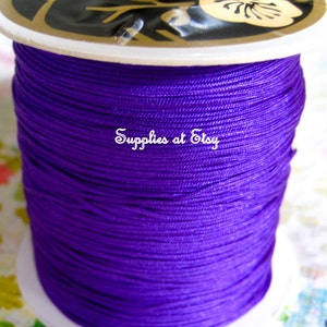 Könnte beinhalten: Eine Spule mit violetter gewachster Schnur, fest auf einer weißen Kunststoffspule mit einem Blumendesign auf der Oberseite gewickelt.