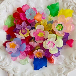 May include: A collection of colorful plastic flower and leaf shapes in a white bowl. The flowers are in shades of pink, red, yellow, orange, blue, and purple. The leaves are green and blue.