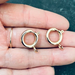 May include: Two gold-toned metal clasps for jewellery making. Each clasp has a round ring and a hook.