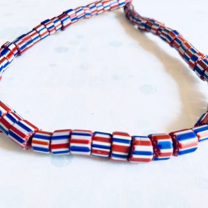 Pode incluir: Um colar feito de contas de vidro vermelho, branco e azul. As contas são cilíndricas e têm um padrão listrado.