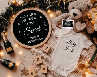 Puede incluir: Un tablero de letras negro con letras blancas que deletrean "We've been keeping a little secret coming August 2025". Un mameluco blanco con texto negro que dice "Baby Smith" y estrellas doradas brillantes. Un oso de peluche, una botella de champán y bloques de madera que deletrean "Baby" también están en la imagen.