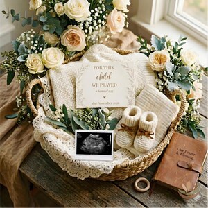 Op de afbeelding: Een rieten mand gevuld met babyartikelen, waaronder een gebreide deken, babyschoentjes en een kaart met de tekst "FOR THIS CHILD WE PRAYED". De mand is omgeven door bloemen en groen, met een echofoto en een klein boek.