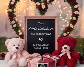 May include: Two pink and red teddy bears sit in front of a chalkboard sign that reads "Two Little Valentines are on their way! Due to arrive August 2025". The sign is decorated with a heart and is surrounded by a heart-shaped floral arrangement with red and pink roses.