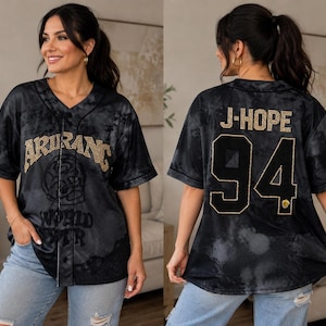 Pu&ograve; includere: Una maglia da baseball nera e grigia con effetto tie-dye, scollo a V e chiusura frontale con bottoni. La parte anteriore presenta la scritta ARIRANG WORLD TOUR in strass dorati. Il retro mostra la scritta J-HOPE e il numero 94 in strass dorati.
