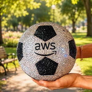 Pu&ograve; includere: Un pallone da calcio sferico ricoperto di strass argentati e neri scintillanti. Il centro del pallone presenta la scritta nera "aws" con una freccia curva sottostante, anch'essa realizzata con piccoli cristalli neri scintillanti.