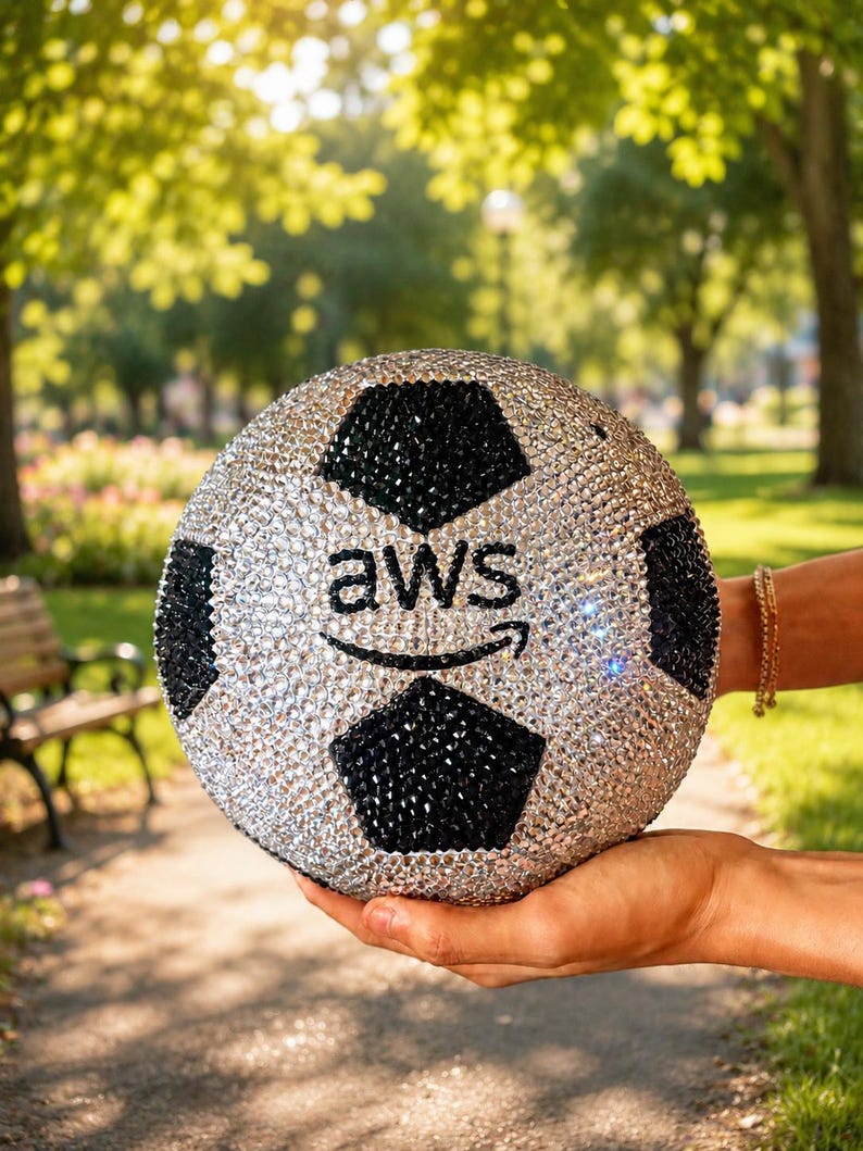 Pu&ograve; includere: Un pallone da calcio sferico ricoperto di strass argentati e neri scintillanti. Il centro del pallone presenta la scritta nera "aws" con una freccia curva sottostante, anch'essa realizzata con piccoli cristalli neri scintillanti.