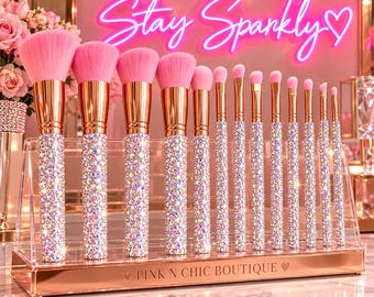 Può includere: Un set di dodici pennelli da trucco con setole rosa brillante, ghiere in oro rosa e manici ricoperti di cristalli iridescenti. I pennelli sono disposti in un supporto in acrilico trasparente con una base in oro rosa con la scritta PINK N CHIC BOUTIQUE.