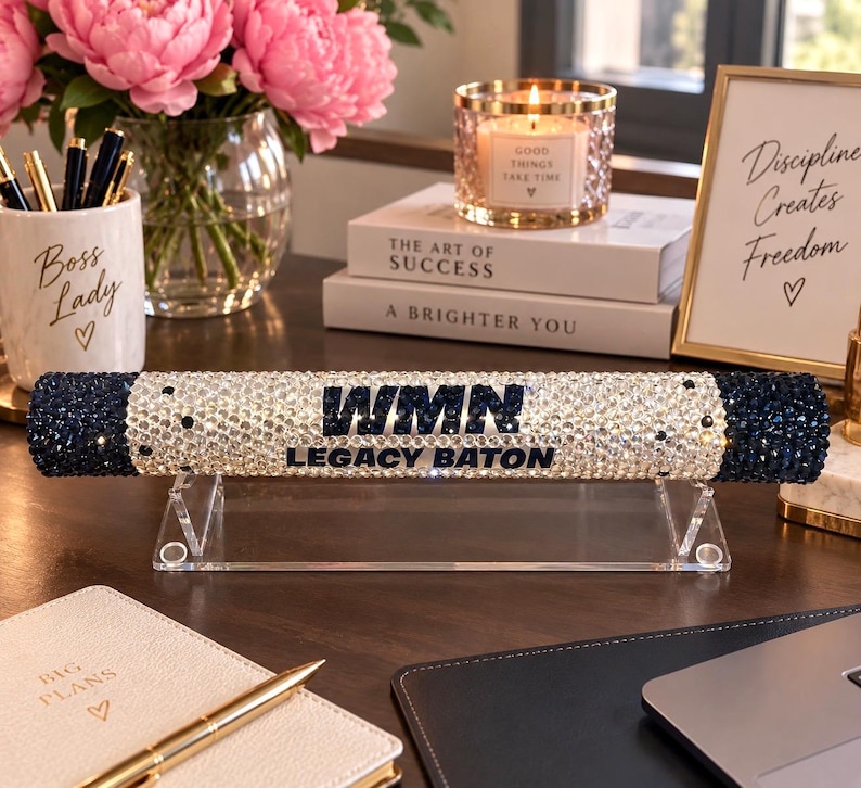 Pu&ograve; includere: Un bastone cilindrico poggiato su un supporto in acrilico trasparente, ricoperto di strass scintillanti trasparenti e blu scuro. Al centro presenta il testo WMN e LEGACY BATON in lettere blu scuro. Le estremit&agrave; sono rifinite con pietre blu scuro.