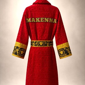 Pu&ograve; includere: Un accappatoio rosso con un motivo logo Versace in rilievo su tutto il tessuto. Il retro mostra il nome MAKENNA in lettere dorate. Include una cintura con motivo nero e oro e polsini abbinati con un motivo a testa di Medusa.