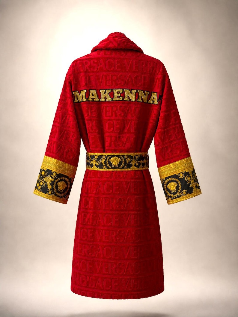 Pu&ograve; includere: Un accappatoio rosso con un motivo logo Versace in rilievo su tutto il tessuto. Il retro mostra il nome MAKENNA in lettere dorate. Include una cintura con motivo nero e oro e polsini abbinati con un motivo a testa di Medusa.