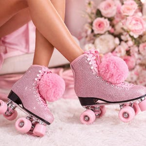 May include: Pink roller skates embellished with rhinestones, with pink pom-poms and laces. The skates have black soles and pink wheels. The image has a soft, feminine aesthetic, with a focus on the skates.