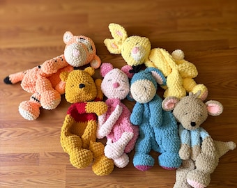 May include: A collection of six plush crochet stuffed animals featuring a yellow bear, a pink piglet, a blue donkey, a yellow rabbit, an orange tiger, and a tan kangaroo. Each soft toy is crafted with a textured yarn finish and embroidered facial features.