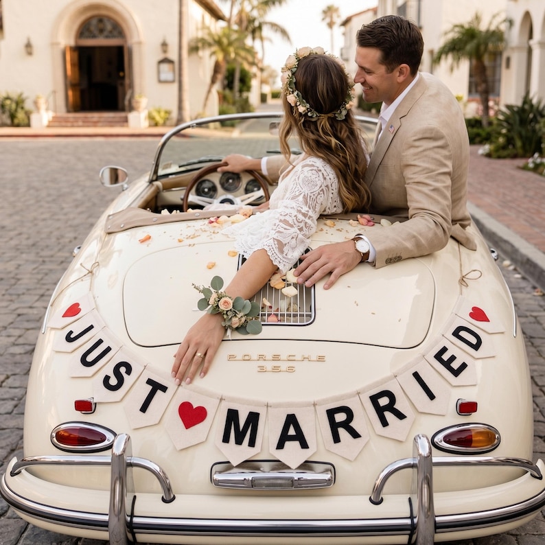 May include: A cream-coloured vintage Porsche 356 convertible decorated with a Just Married banner featuring red hearts and black lettering. The car is adorned with scattered flower petals, and the rear deck lid displays the Porsche 356 emblem.