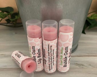May include: Four cylindrical tubes of Bubble Gum lip balm with clear caps. Three tubes stand upright, and one lies horizontally. The labels feature a pink bubble pattern and text reading Royal Belle Studios Bubble Gum Lip Balm.