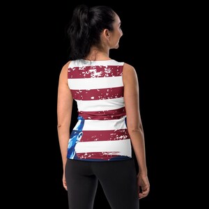 K&ouml;nnte beinhalten: Ein wei&szlig;es Tanktop mit einem abgenutzten amerikanischen Flaggenmuster. Die Flagge ist rot, wei&szlig; und blau mit einem verblassten Look. Das Tanktop hat einen runden Ausschnitt und ist &auml;rmellos.
