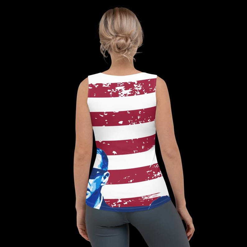 K&ouml;nnte beinhalten: Ein wei&szlig;es Tanktop mit einem rot-wei&szlig;-blauen amerikanischen Flaggenmuster. Die Flagge hat einen abgenutzten Look und zeigt eine blaue Silhouette einer Person mit Sonnenbrille.
