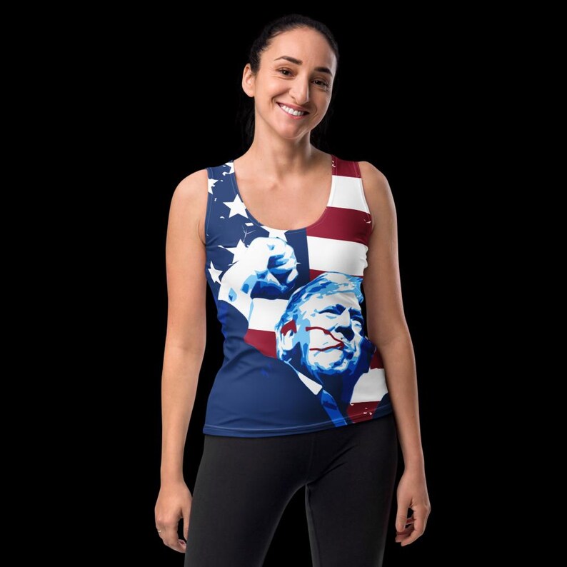 K&ouml;nnte beinhalten: Ein blaues Tanktop mit einem grafischen Druck einer Person mit erhobener Faust und einem amerikanischen Flaggenhintergrund. Das Gesicht der Person ist teilweise vom Flaggenmuster verdeckt.