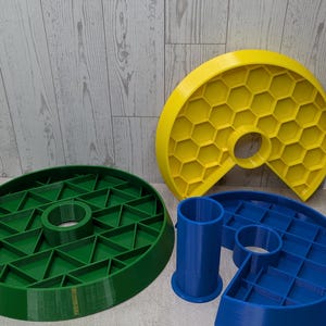 May include: A collection of 3D-printed geometric shapes in various colors. Includes a green circular piece with a central hole, a yellow honeycomb-patterned piece, and blue cylindrical and semi-circular components. A small blue dome is also present.