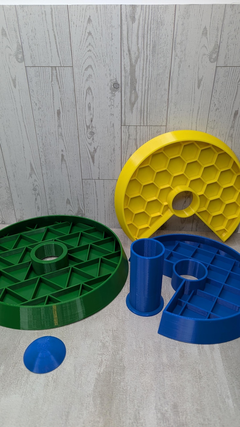 May include: A collection of 3D-printed geometric shapes in various colors. Includes a green circular piece with a central hole, a yellow honeycomb-patterned piece, and blue cylindrical and semi-circular components. A small blue dome is also present.