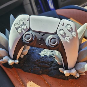 Op de afbeelding: Een witte en zwarte gamecontroller met een unieke kristalachtige basis. De controller heeft een strak ontwerp met knoppen en joysticks. De basis is donkergrijs met lichtgrijze kristalaccenten.