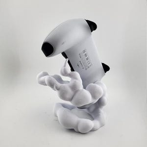 Op de afbeelding: Een wit en zwarte gamecontroller op een witte, wolkvormige standaard. De controller is omhoog gekanteld en wordt ondersteund door de standaard. De standaard heeft een gestructureerd, organisch ontwerp.