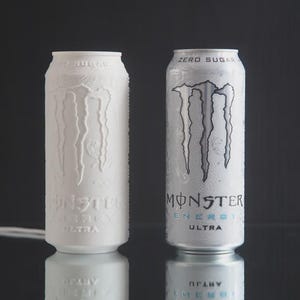 May include: Two Monster Energy Ultra cans are displayed. One is a solid white, embossed with the Monster logo. The other is a silver can with the Monster logo in black and blue, with the words "ZERO SUGAR" at the top.