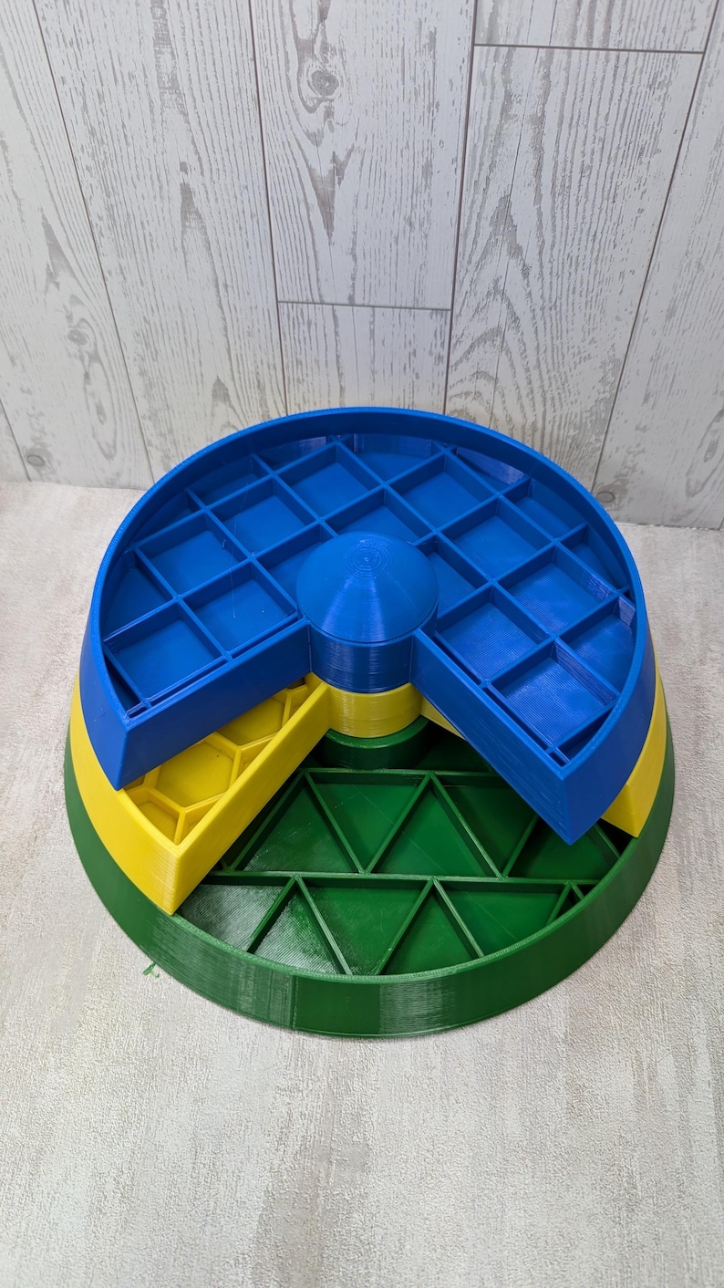 May include: A multi-tiered, 3D-printed organizer in primary colors. The base is green, supporting a yellow layer with hexagonal compartments. A blue top layer features a grid of square compartments. The organizer is designed for small items.