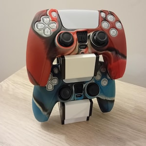 May include: Two game controllers stacked on top of each other. The top controller is red and black with white accents. The bottom controller is blue and black with white accents. Both controllers have black buttons and a white center.