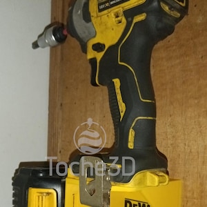 Peut inclure: Un tournevis à percussion DeWalt 18V XR Brushless Motor jaune et noir avec une batterie noire et jaune montée sur un support mural jaune. Le support mural porte l'inscription "DEWA".