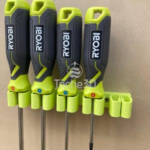 Peut inclure: Un porte-tournevis vert et noir avec quatre tournevis Ryobi. Le porte-tournevis a quatre fentes pour les tournevis et est en plastique. Les tournevis sont tous de la même taille et ont une poignée noire avec une pointe verte.