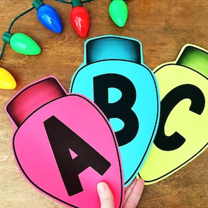 May include: Colorful Christmas light-shaped cutouts with the letters A, B, and C in black. The cutouts are pink, blue, and yellow. A string of Christmas lights with blue, red, green, and yellow bulbs is in the background.