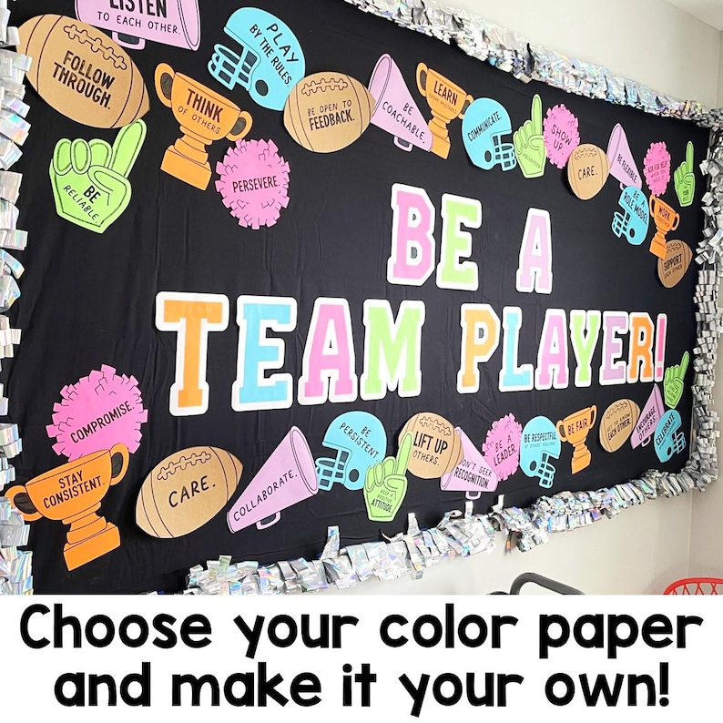 May include: A black bulletin board display featuring the text BE A TEAM PLAYER in large colorful letters. The board is decorated with cutouts of footballs, trophies, megaphones, foam fingers, and pom-poms, each printed with motivational phrases.