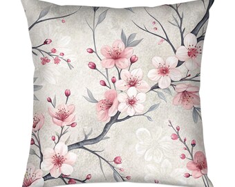 May include: Square decorative pillow featuring a watercolor floral design. The pillow has a light beige background with a pattern of pink cherry blossoms, buds, and gray branches. The blossoms have a delicate, soft appearance.