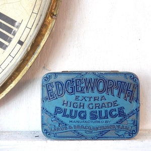May include: A blue and white tin with the text "Edgeworth Extra High Grade Plug Slice" and "Manufactured by Larus & Bro. Co. Richmond, Va. U.S.A."