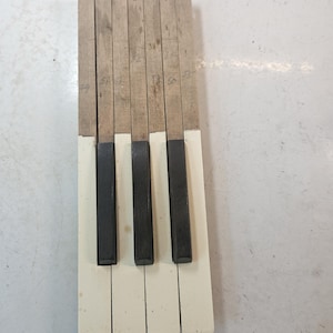 May include: A section of piano keys, featuring a combination of white and black keys. The keys are made of wood and have a worn appearance. Numbers are written on the wooden portion of the keys. The keys are arranged in a row, suggesting a musical instrument.