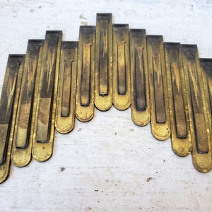 May include: A collection of antique brass metal pieces arranged in an arch shape. Each piece is rectangular with a rounded bottom and a darker, aged patina. The arrangement suggests a decorative or architectural element.