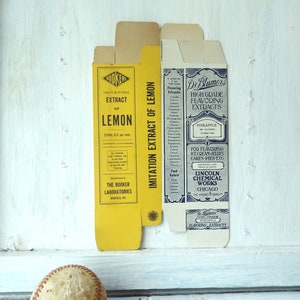 May include: Vintage extract boxes for lemon and pineapple flavoring. The yellow box reads "Imitation Extract of Lemon" and the blue box reads "High Grade Flavoring Extracts". A worn baseball with red stitching rests in the foreground.