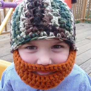Puede incluir: Un ni&ntilde;o con un gorro de punto de camuflaje y una barba de punto naranja a juego.