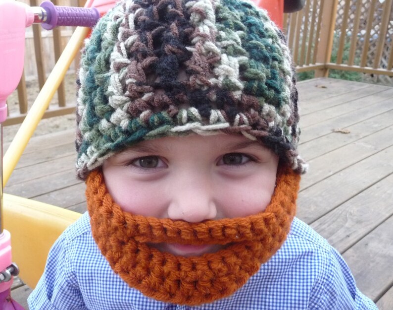 Puede incluir: Un ni&ntilde;o con un gorro de punto de camuflaje y una barba de punto naranja a juego.
